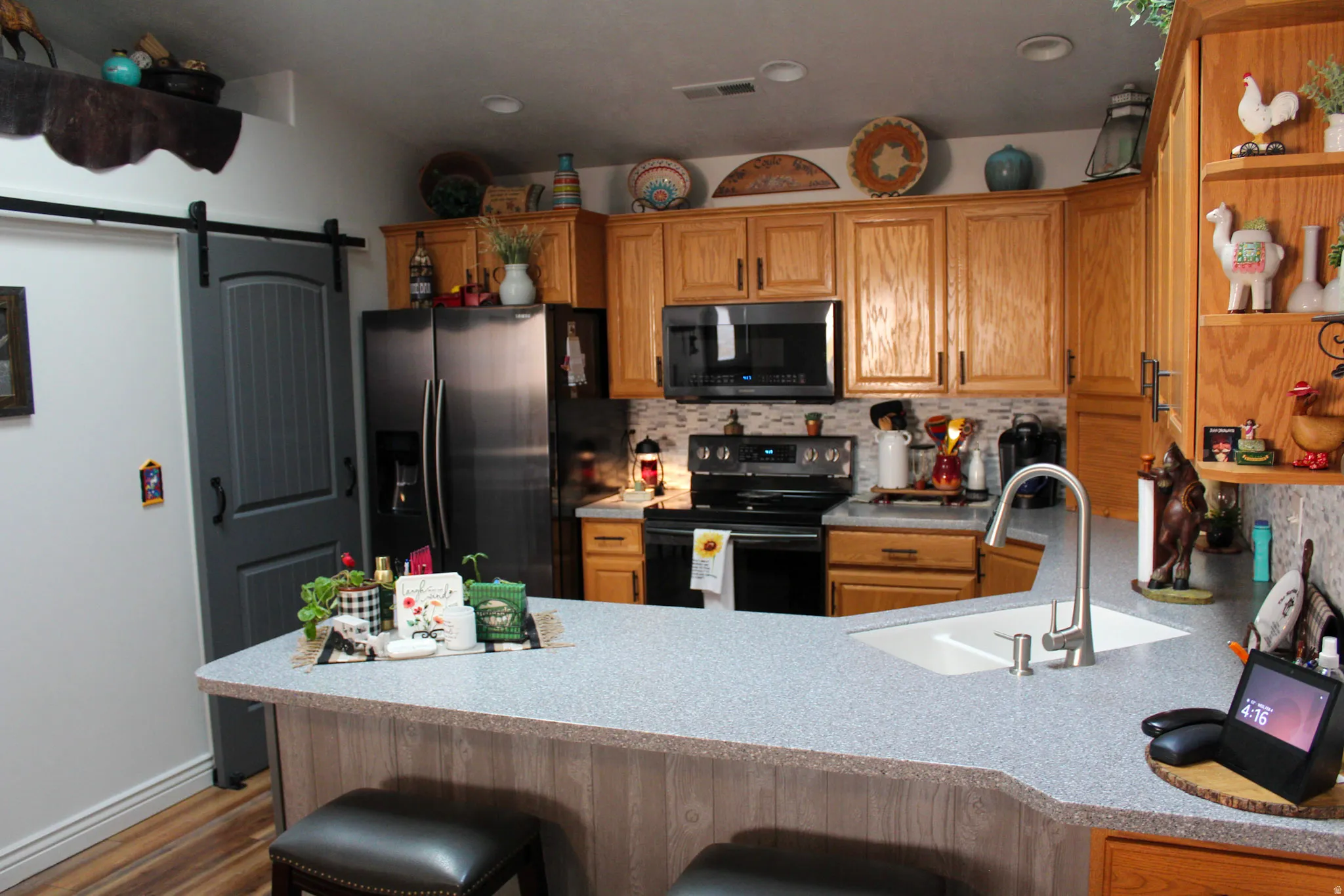 Kitchen featuring a barn door, a kitchen bar, black appliances, open shelves, and decorative backsplash