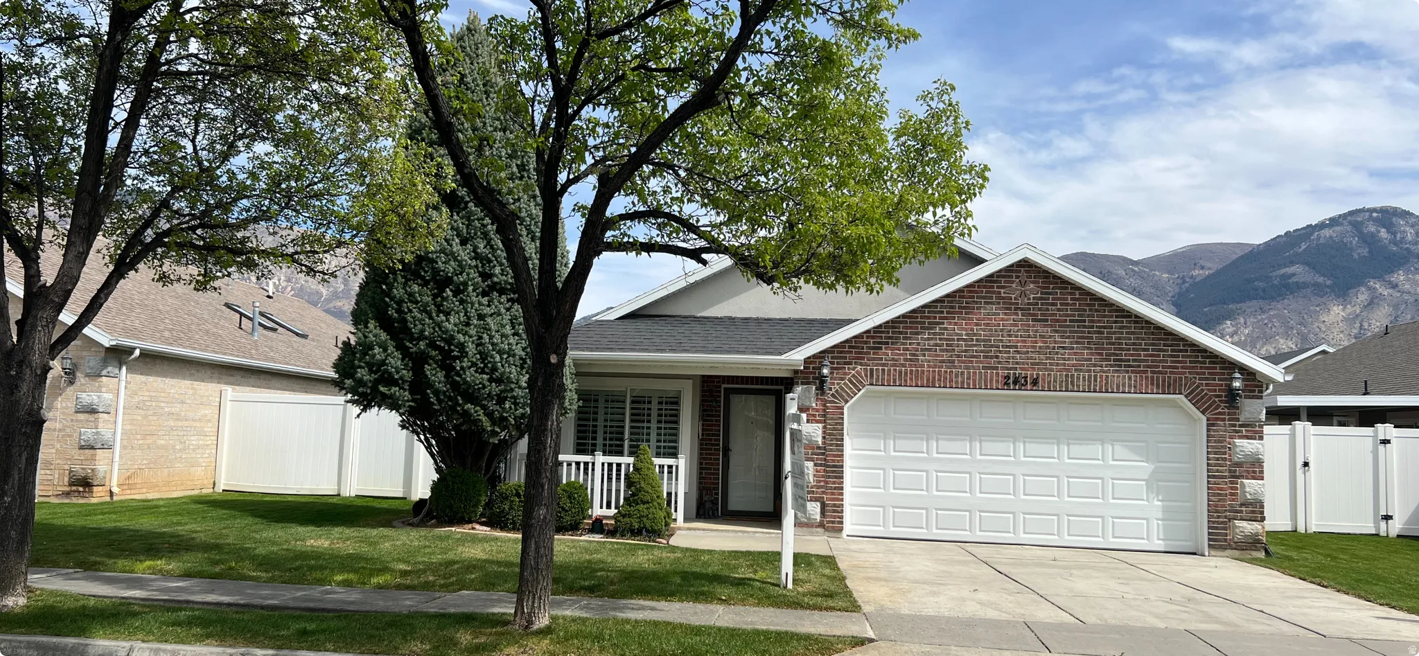 Single story home with an attached garage, driveway, a gate, brick siding, and a mountain view