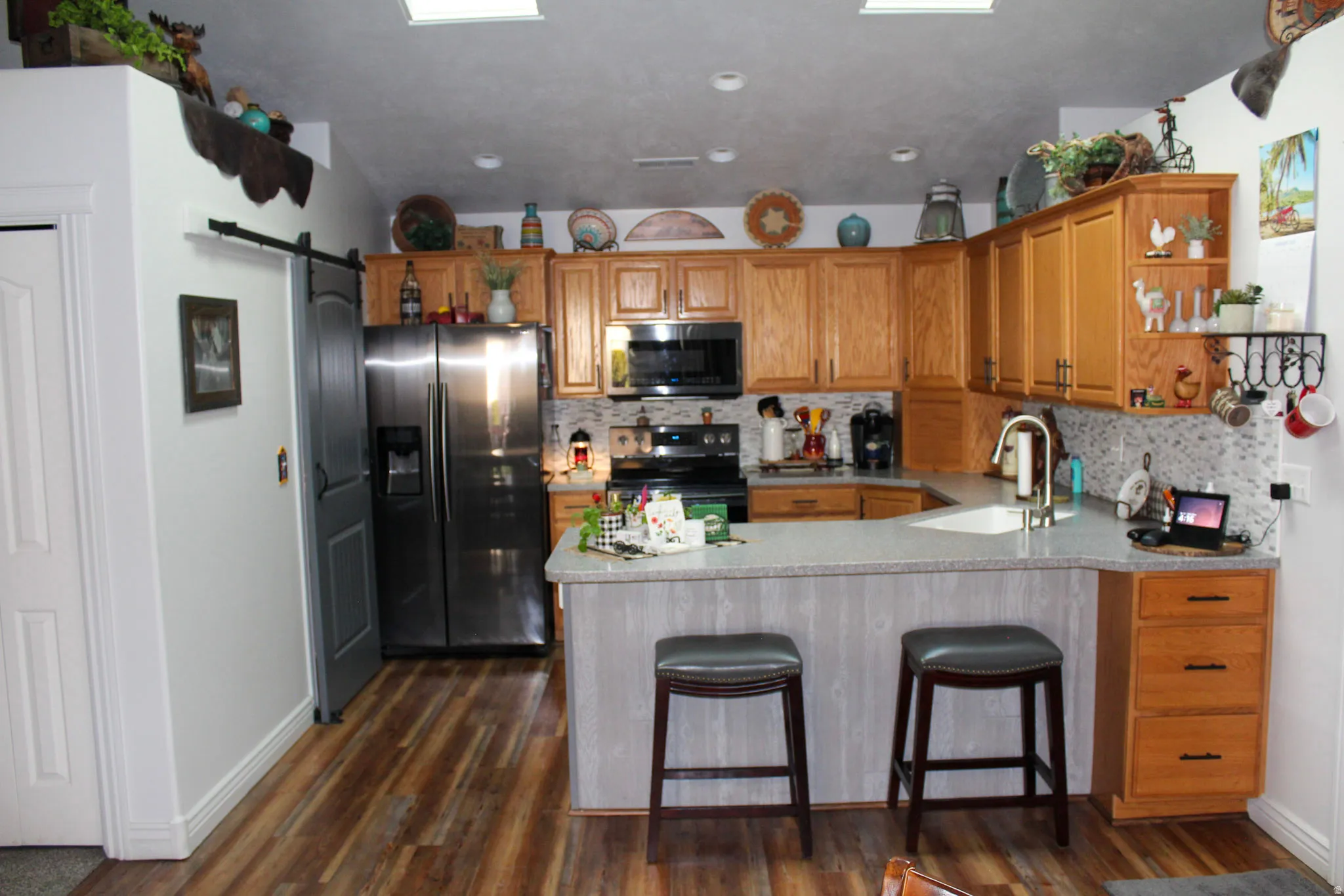 Kitchen featuring a barn door, stainless steel appliances, open shelves, a peninsula, and a breakfast bar area