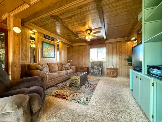 Living area with wood ceiling, wooden walls, light colored carpet, and a ceiling fan