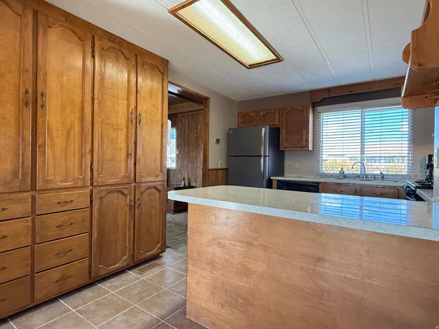 Kitchen featuring wood finish cabinetry, a textured ceiling, freestanding refrigerator, light countertops, and wainscoting