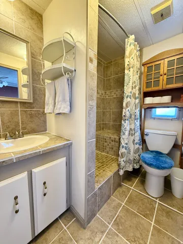 Full bath featuring a shower stall, vanity, a textured ceiling, light tile patterned flooring, and backsplash