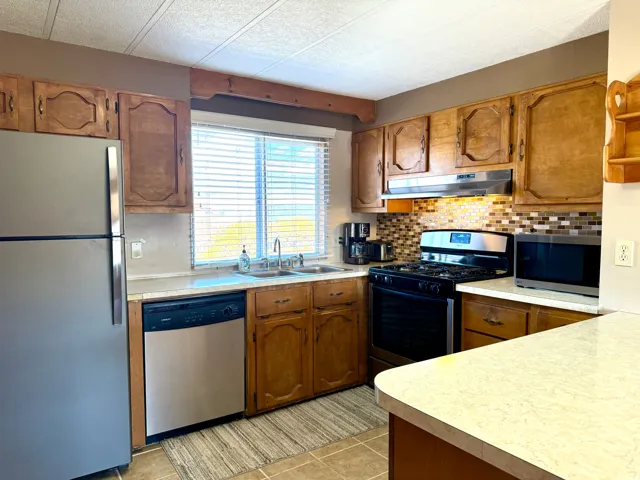 Kitchen with stainless steel appliances, wood finish cabinets, light countertops, backsplash, and a textured ceiling