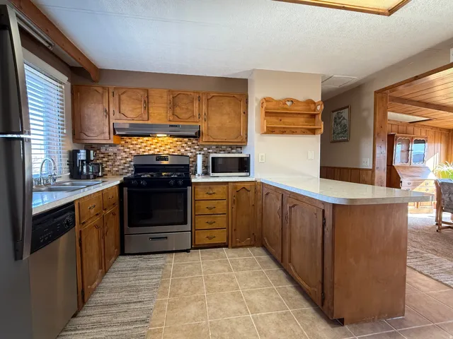 Kitchen with stainless steel appliances, wood finish cabinets, a peninsula, light countertops, and light tile patterned flooring
