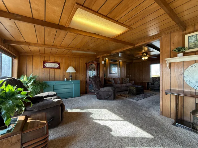 Carpeted living area featuring a wooden ceiling with exposed beams, wooden walls, and a ceiling fan