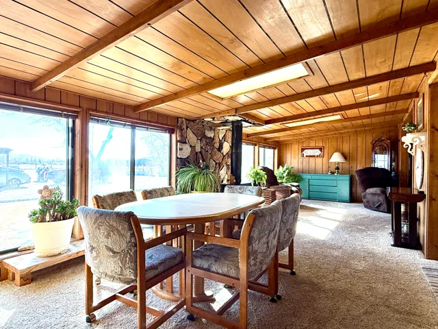 Dining space featuring carpet flooring, a wood ceiling with exposed beams, a wood stove, and wood walls