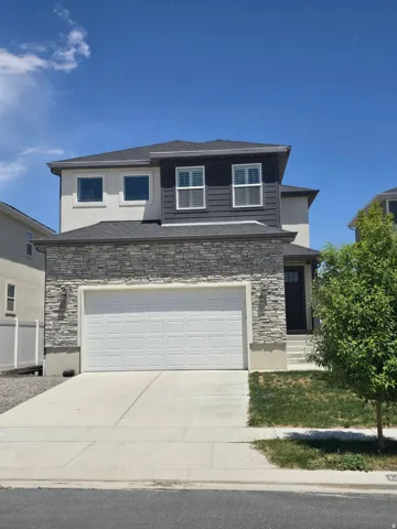 View of front facade with stone siding, an attached garage, and driveway