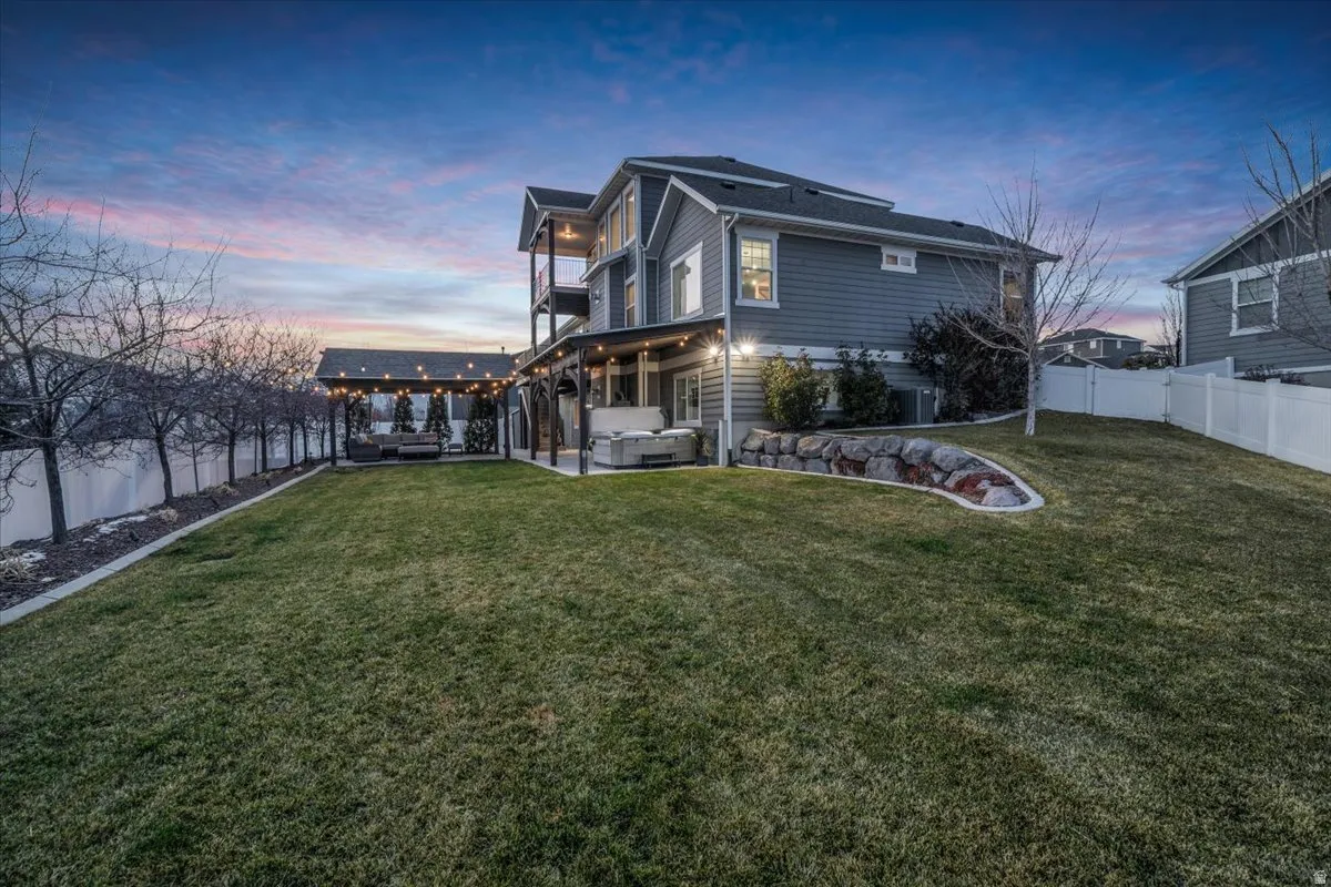 Back of property at dusk with a fenced backyard, an outdoor hangout area, a patio, and a balcony