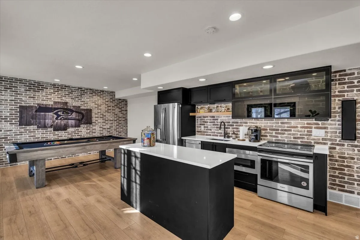 Kitchen with brick wall, dark cabinets, stainless steel appliances, a center island, and glass insert cabinets