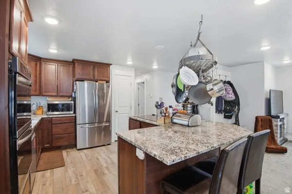 Kitchen with stainless steel appliances, light stone counters, a breakfast bar area, a center island, and recessed lighting