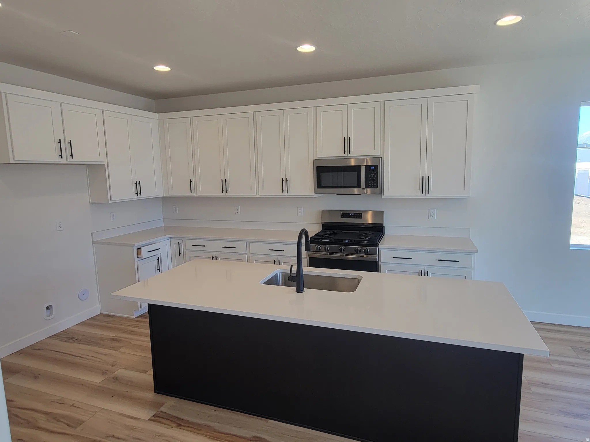 Dual tone kitchen featuring stainless steel appliances, an island with sink, dual tone cabinetry, light wood-type flooring, and recessed lighting