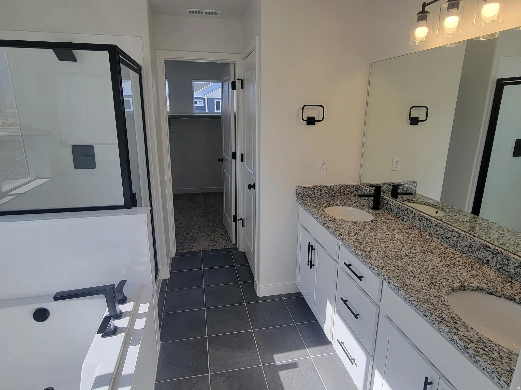 Full bathroom with a bath, a shower stall, double vanity, dark tile patterned floors, and a spacious closet