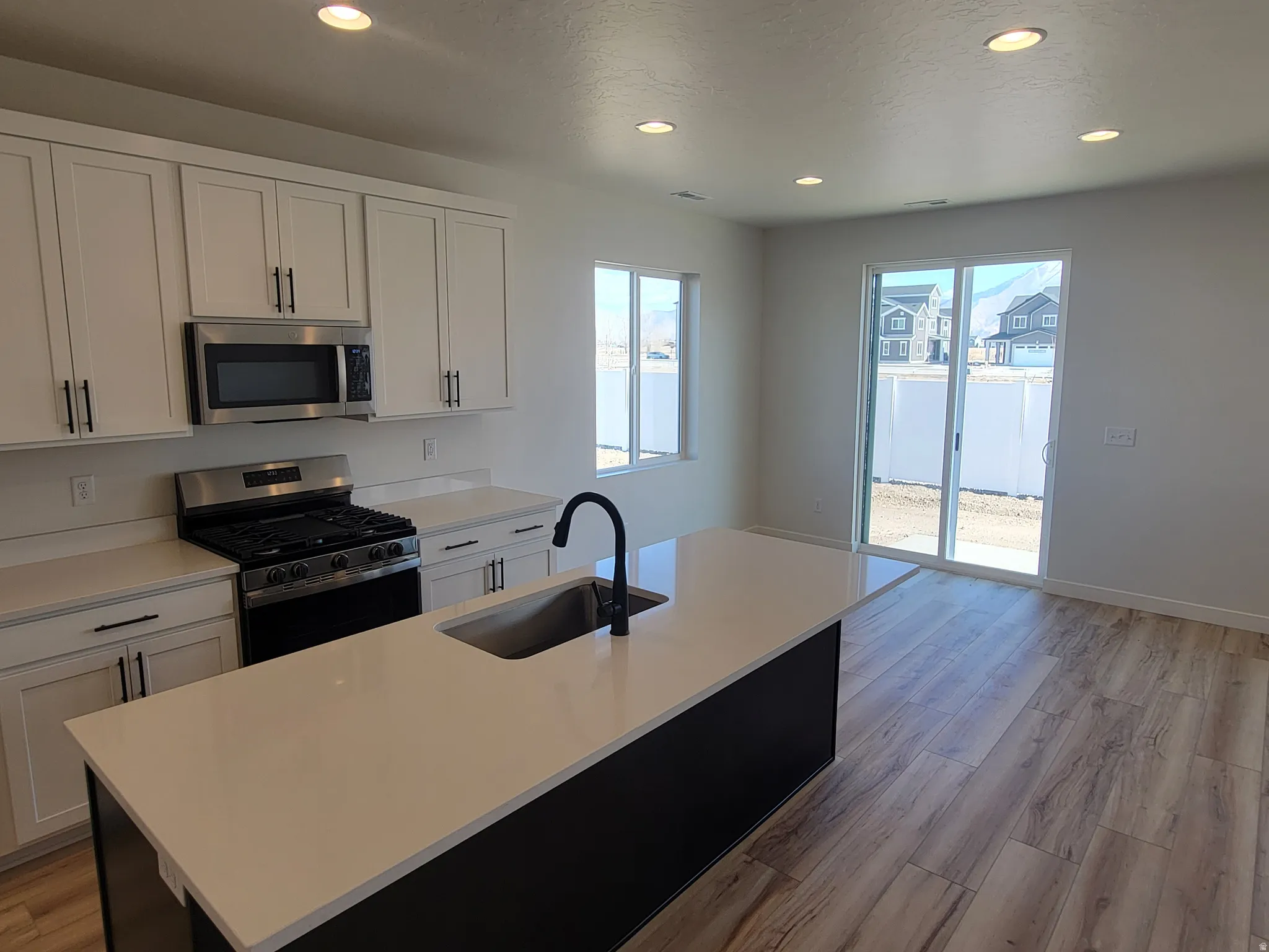 Dual tone kitchen featuring stainless steel appliances, light wood-style floors, recessed lighting, a center island with sink, and light stone counters