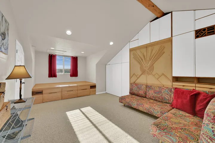 Carpeted room featuring a built-in wooden platform with integrated drawers, recessed lighting, and a window with red drapes