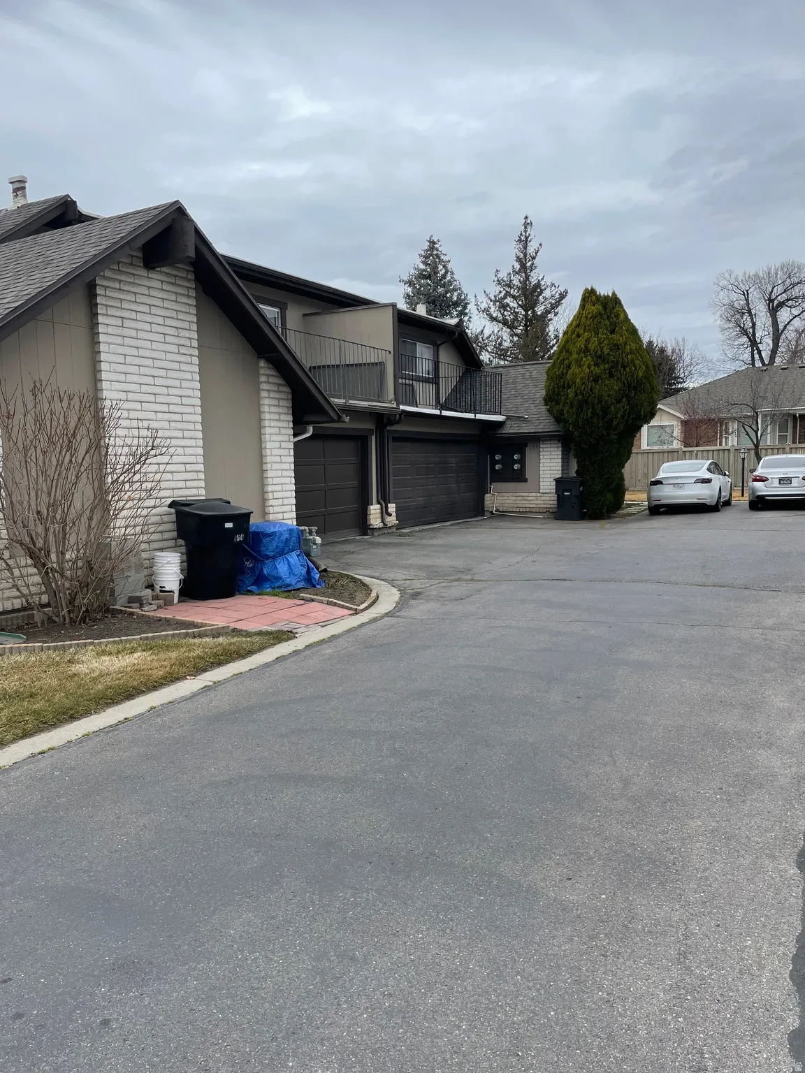 View of side of home with a balcony, brick siding, asphalt driveway, and a garage