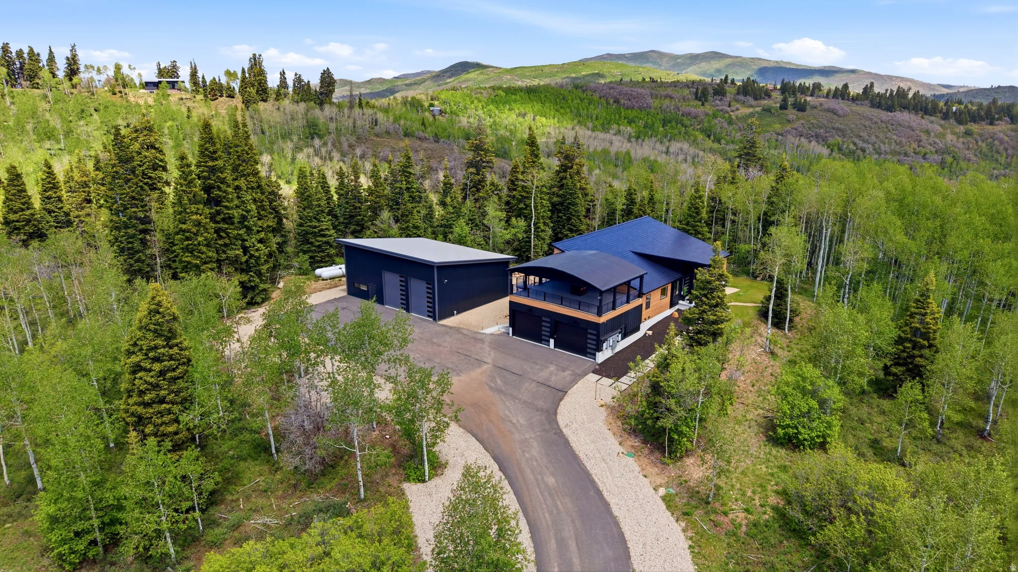 Contemporary residence featuring a dark-toned exterior with wood accents and a curved balcony, situated on a sloped lot