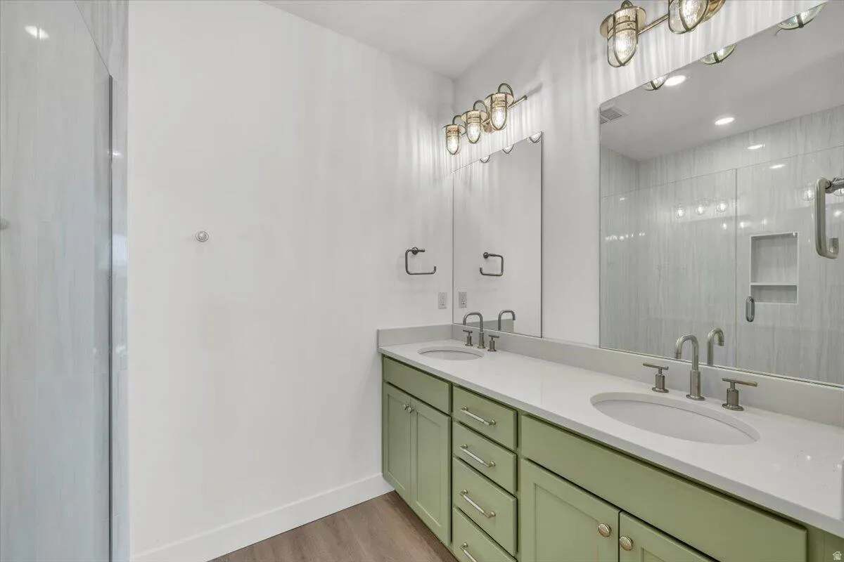 Full bath with double vanity, tiled shower, light wood-type flooring, and recessed lighting