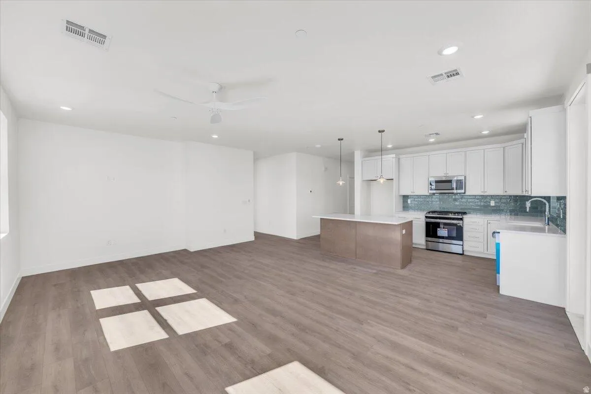 Dual tone kitchen featuring open floor plan, stainless steel appliances, hanging light fixtures, ceiling fan, and light wood finished floors