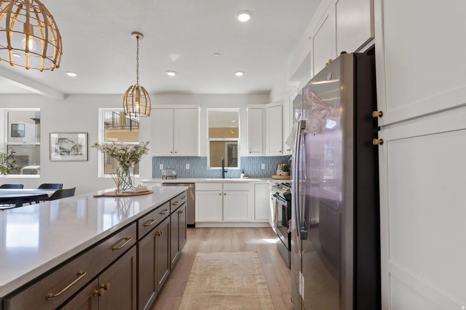 Kitchen with two tone cabinets, stainless steel appliances, hanging light fixtures, light wood finished floors, and light stone countertops