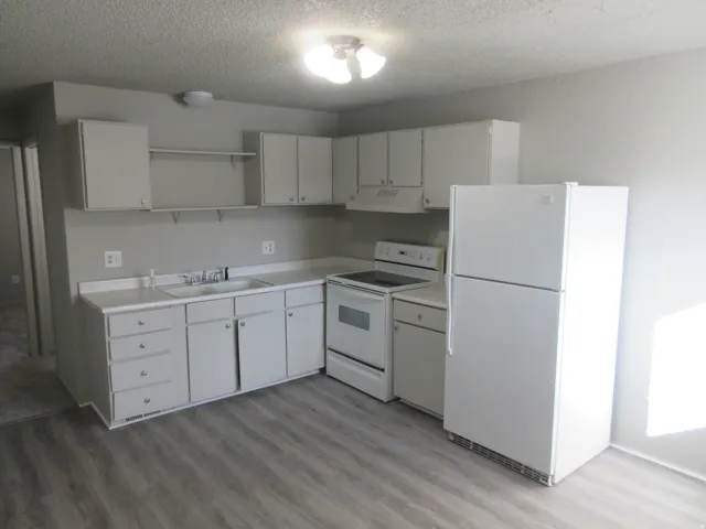 Kitchen featuring white appliances, white cabinetry, open shelves, light countertops, and a textured ceiling