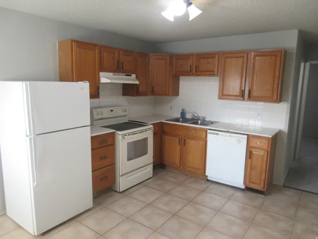 Kitchen with white appliances, wood finish cabinetry, a textured ceiling, backsplash, and light tile patterned floors