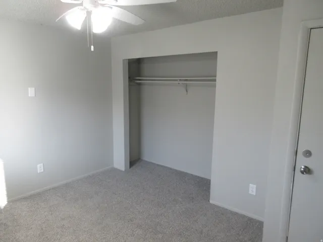 Unfurnished bedroom featuring light colored carpet, a textured ceiling, a ceiling fan, and a closet