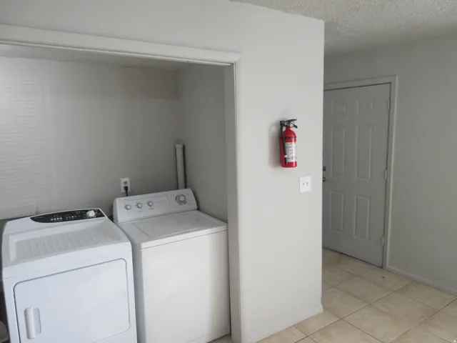 Laundry area with independent washer and dryer, a textured ceiling, and light tile patterned floors