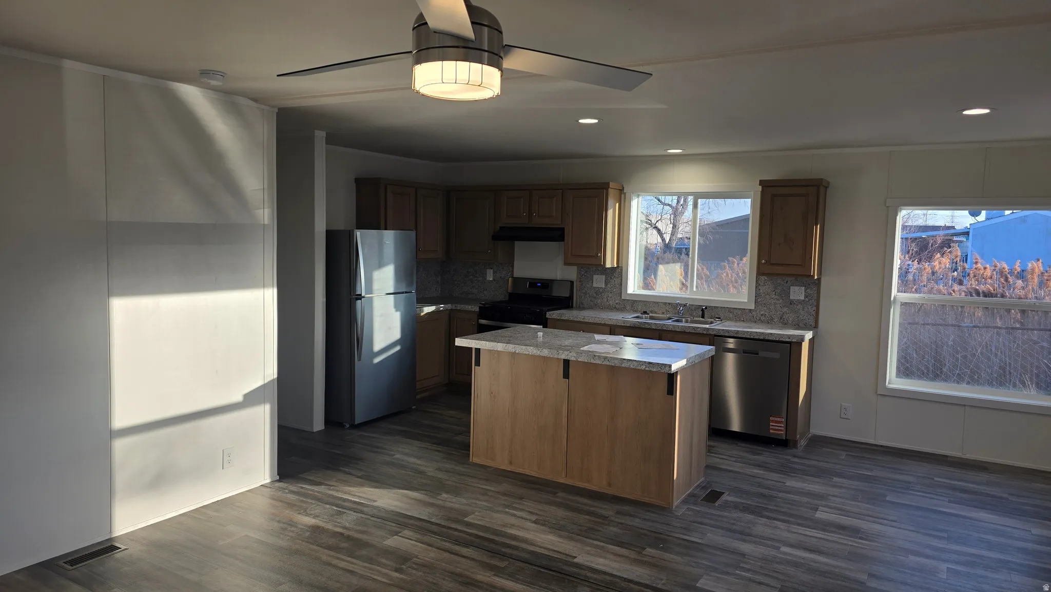 Kitchen featuring stainless steel appliances, light countertops, a ceiling fan, a kitchen island, and tasteful backsplash