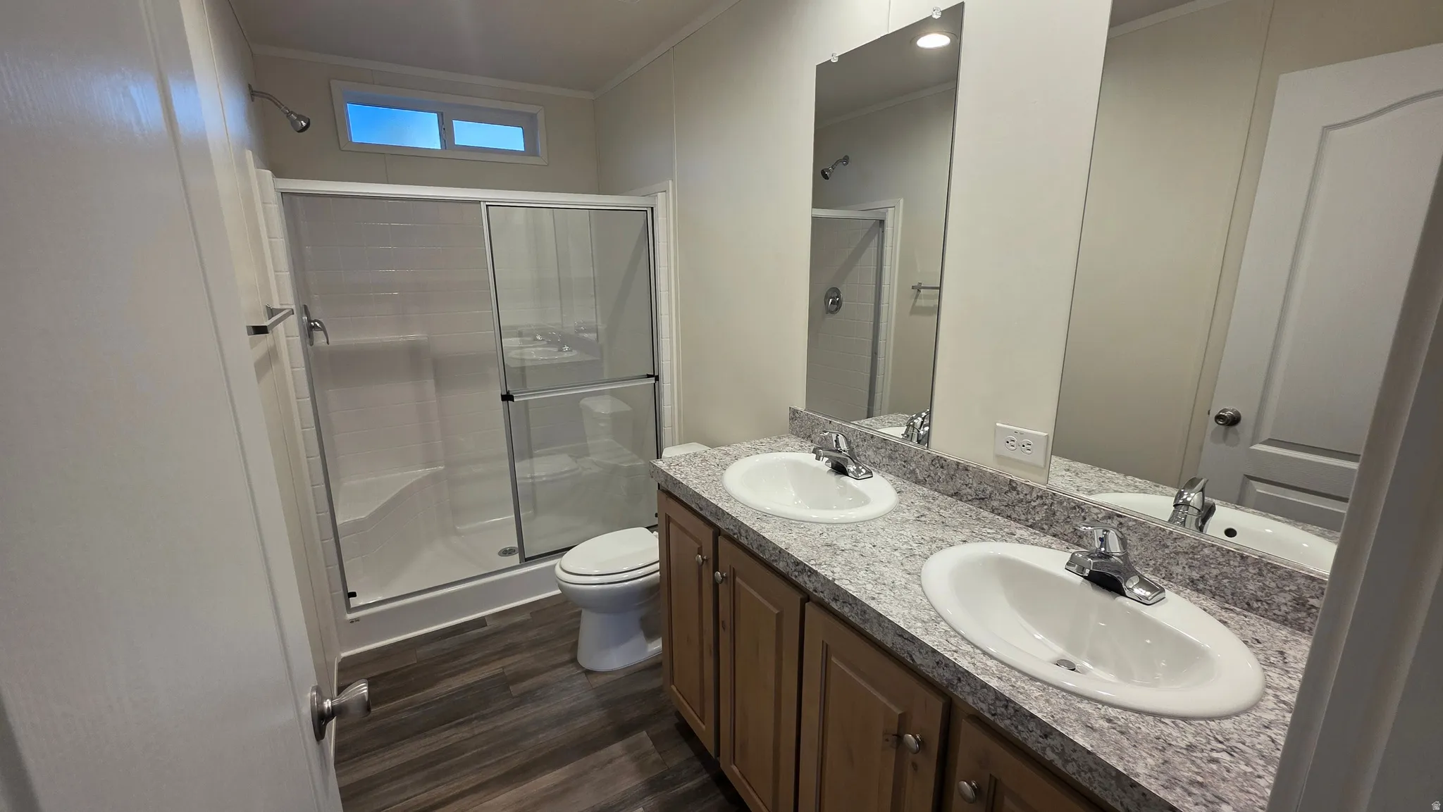 Full bathroom with double vanity, a stall shower, crown molding, and dark wood-type flooring