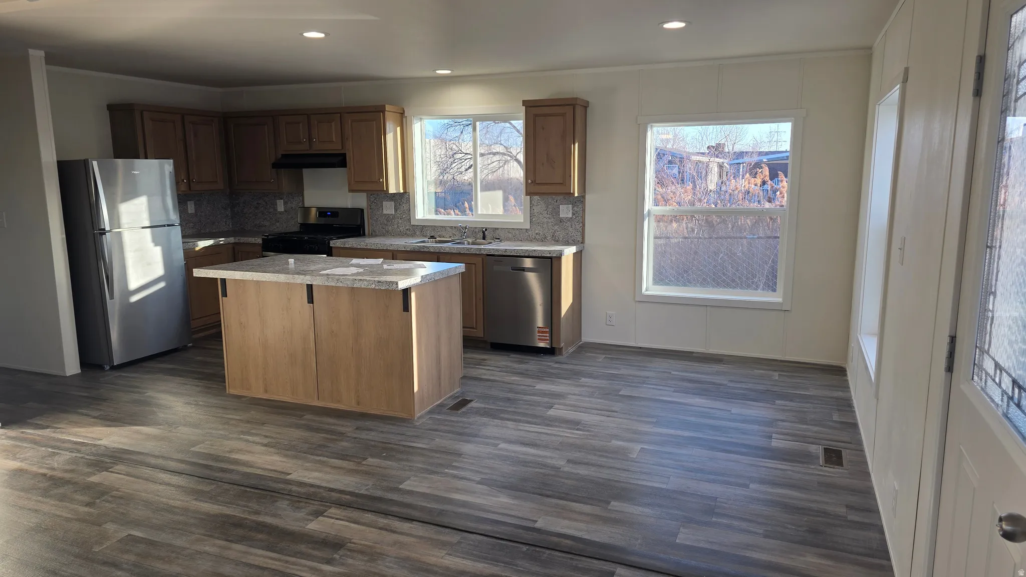Kitchen featuring light countertops, stainless steel appliances, tasteful backsplash, a center island, and dark wood-style floors