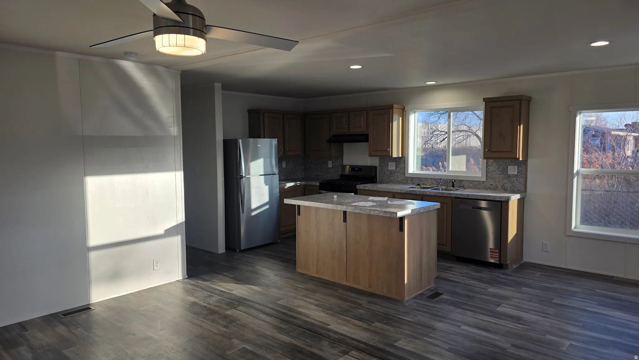 Kitchen with ceiling fan, stainless steel appliances, light countertops, a center island, and dark wood-style flooring
