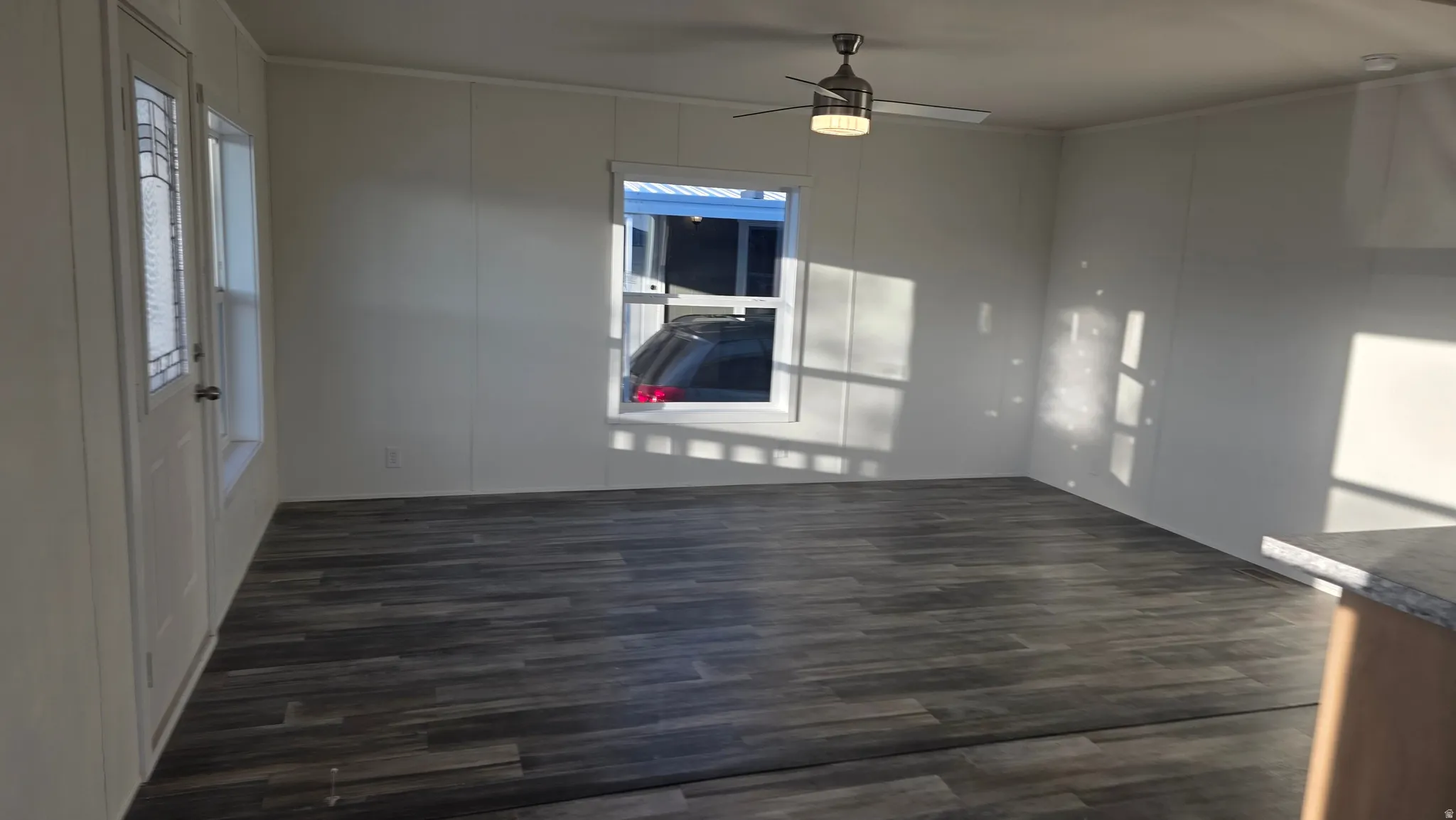 Unfurnished room featuring dark wood finished floors, ceiling fan, plenty of natural light, and a decorative wall