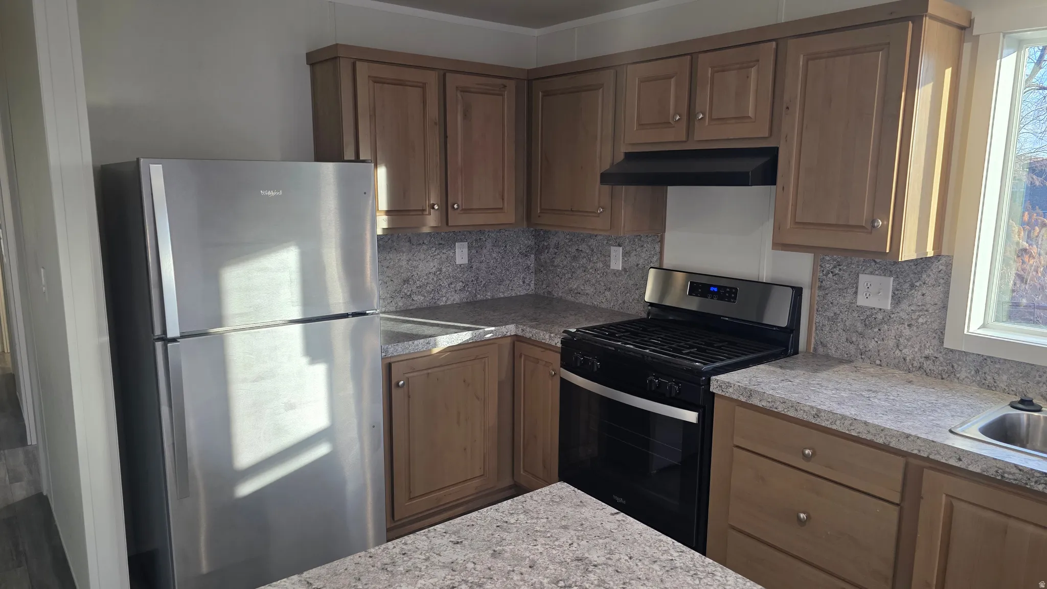 Kitchen featuring stainless steel appliances, decorative backsplash, light countertops, range hood, and wood finish cabinetry
