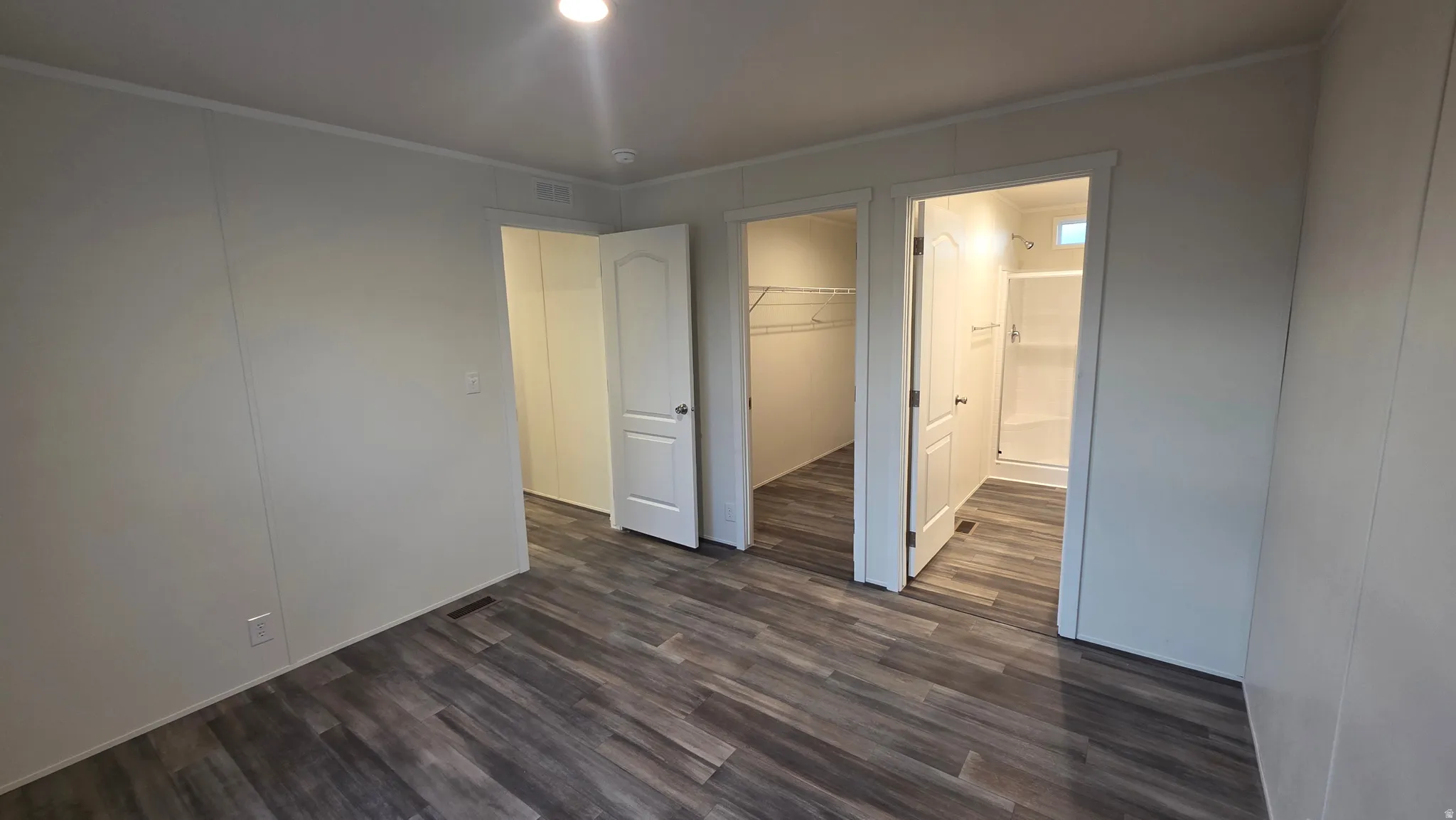 Unfurnished bedroom with dark wood-style floors, a spacious closet, crown molding, and connected bathroom