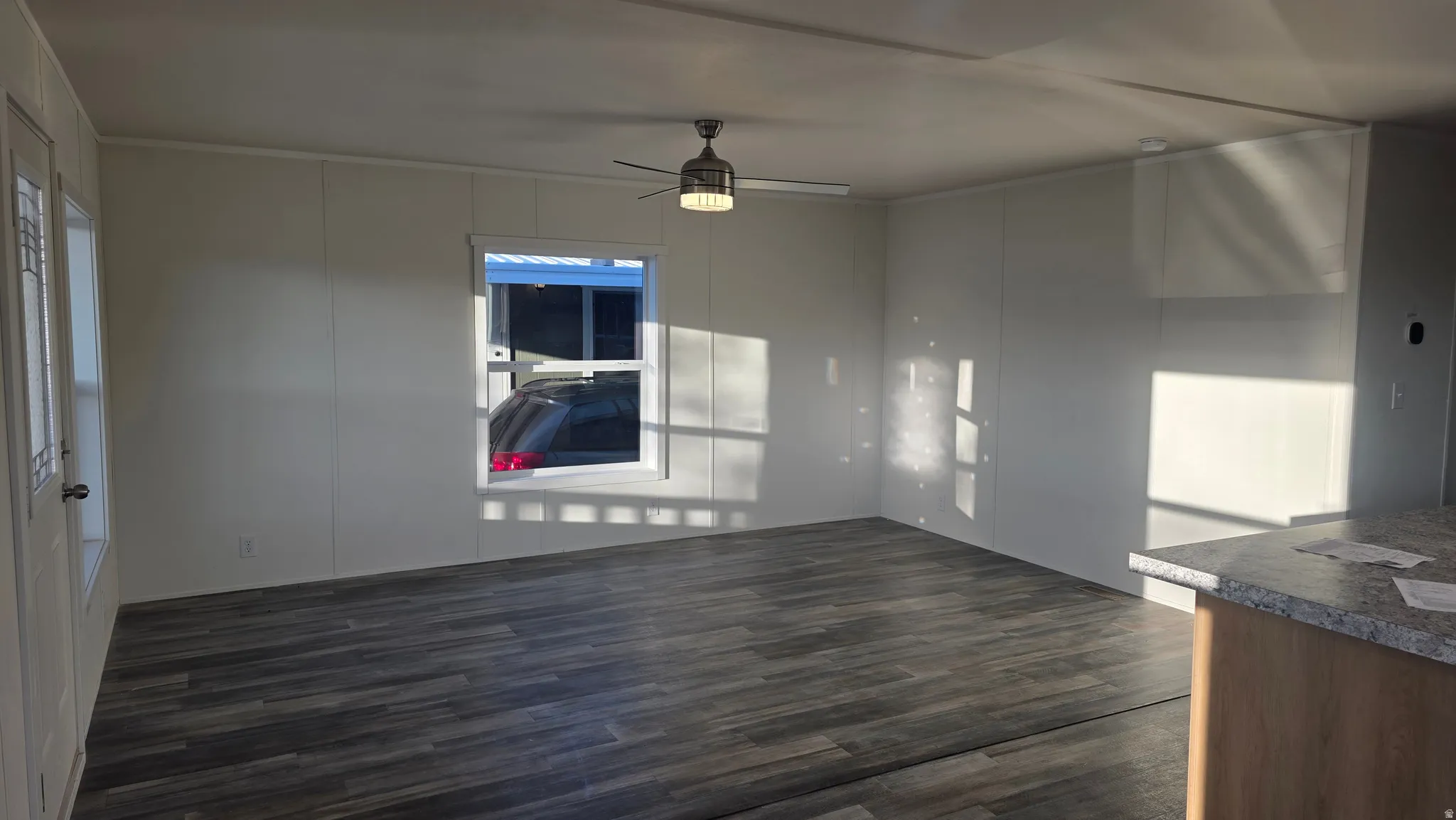 Unfurnished living room featuring dark wood-style floors, a ceiling fan, and healthy amount of natural light