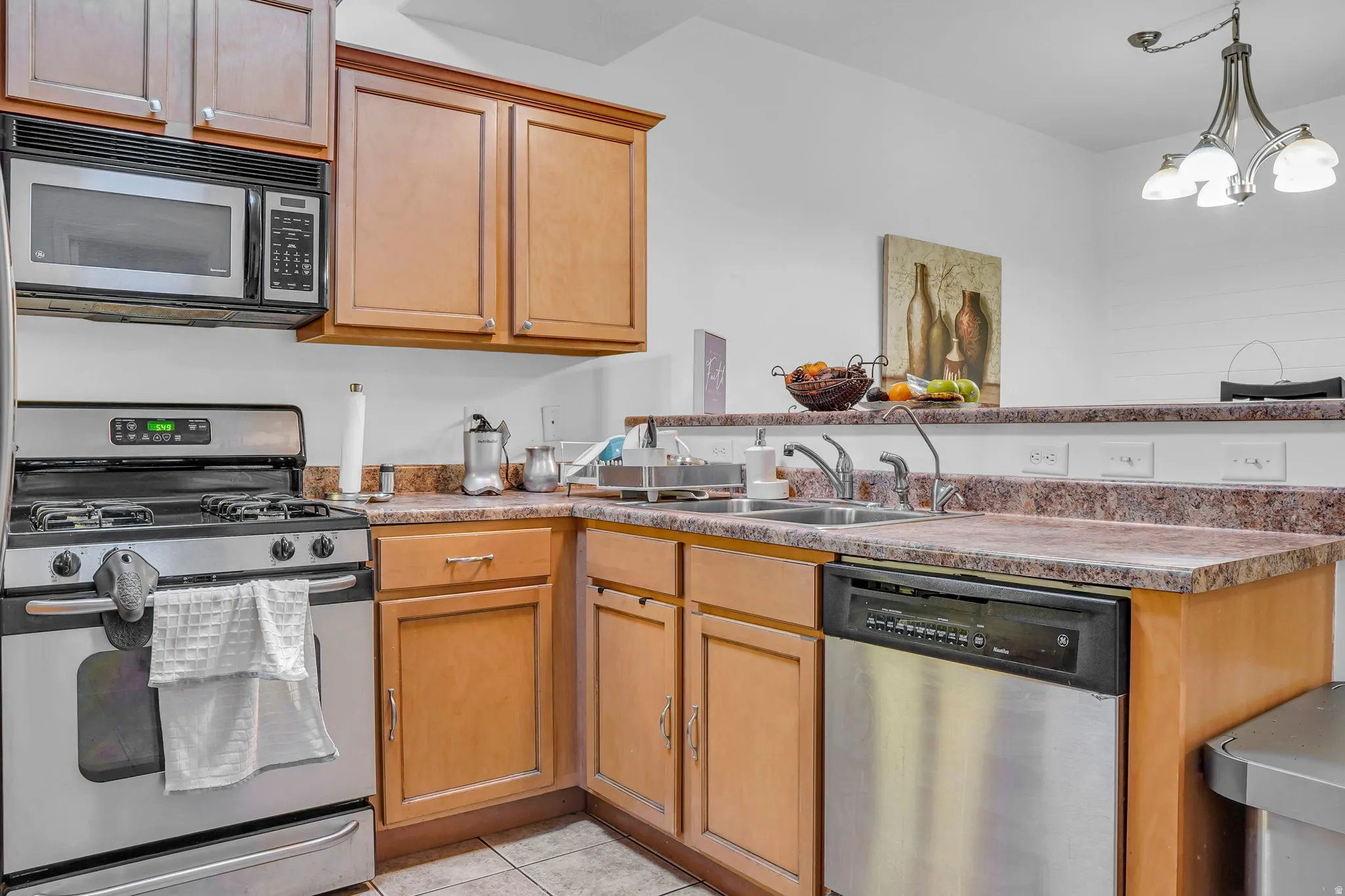 Kitchen with stainless steel appliances, a peninsula, suspended lighting, light tile patterned floors, and light countertops