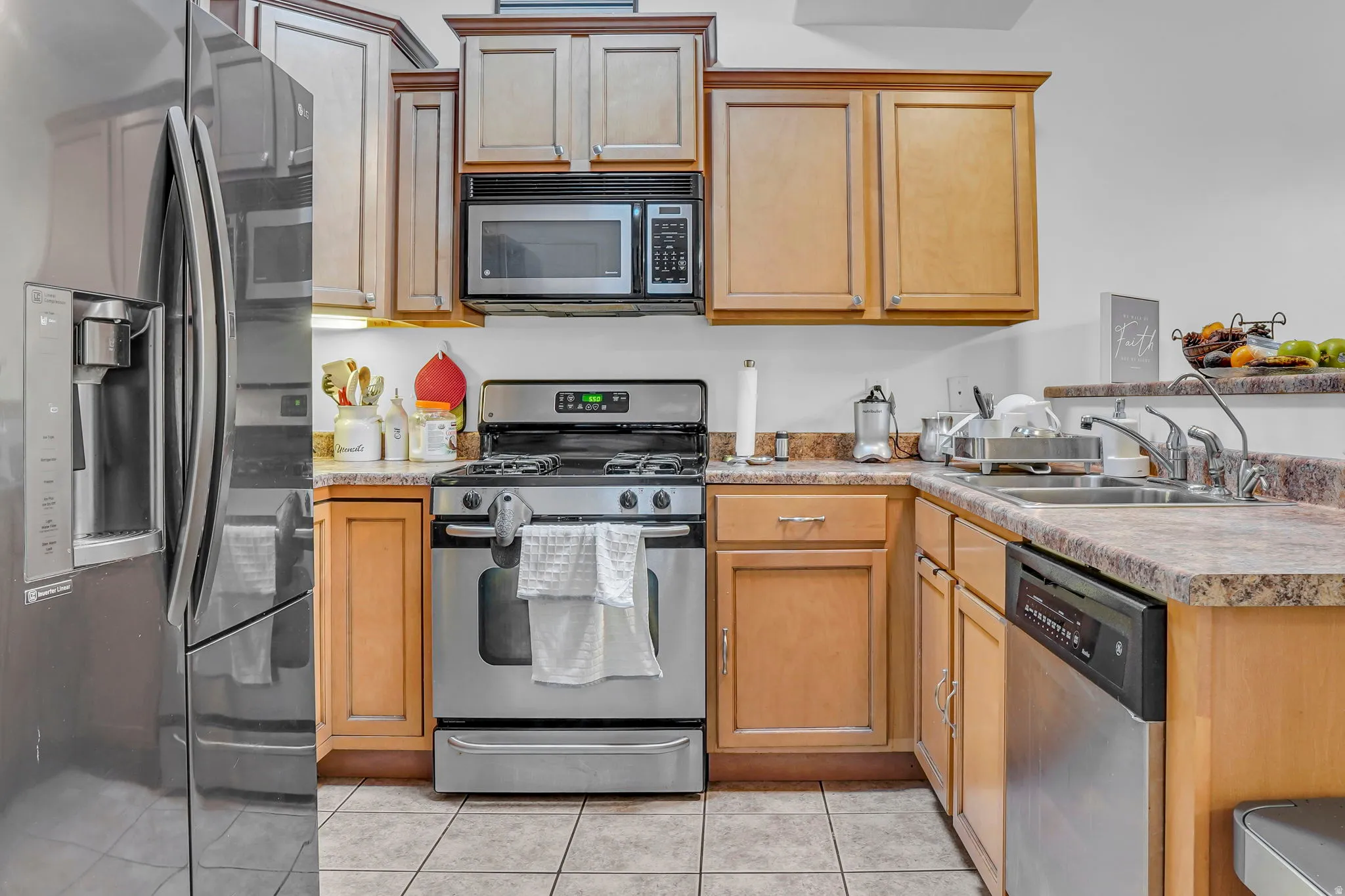 Kitchen with stainless steel appliances, light countertops, light tile patterned flooring, and a peninsula