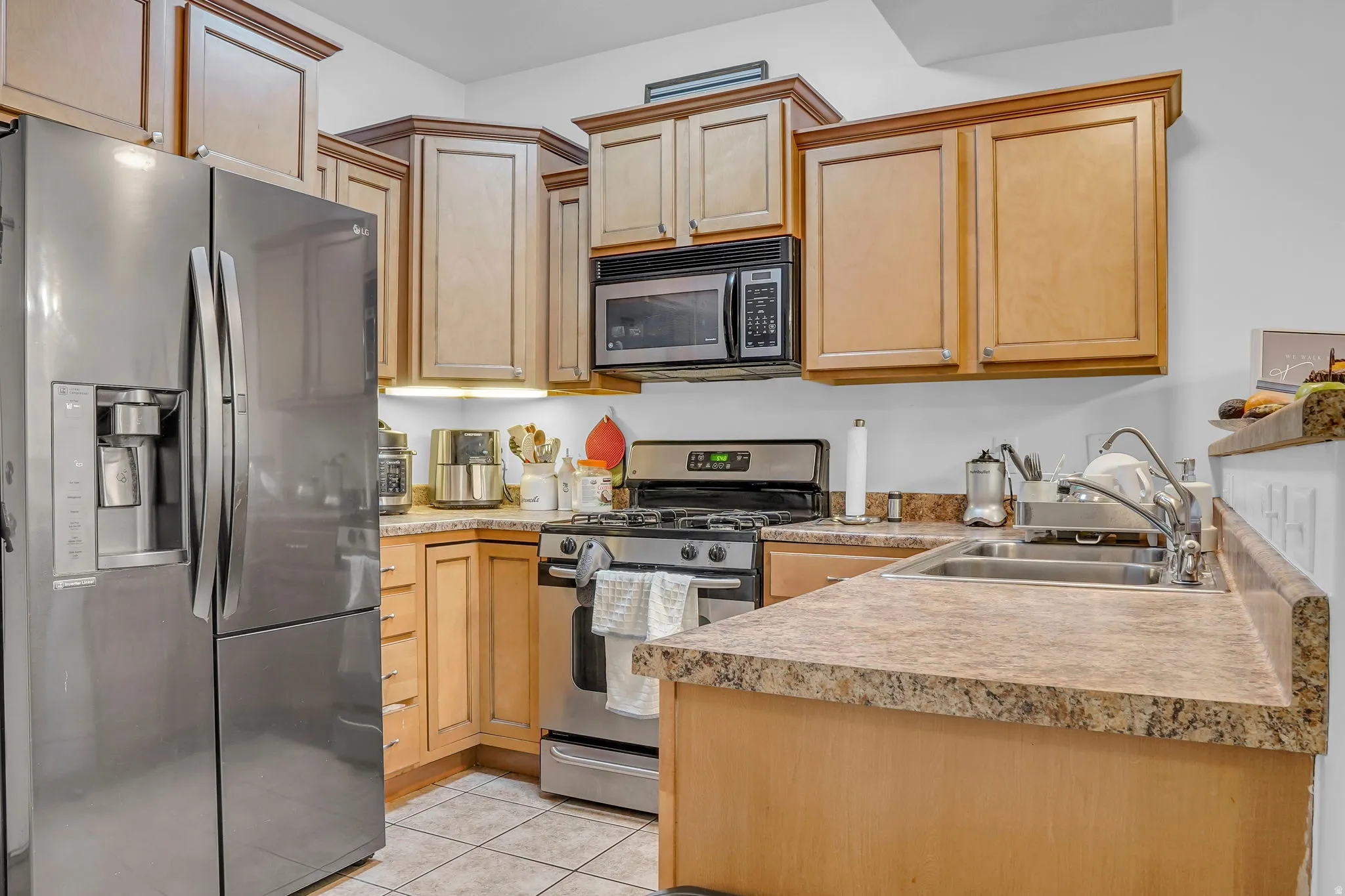 Kitchen featuring stainless steel appliances, light countertops, a peninsula, light tile patterned flooring, and light wood finish cabinets