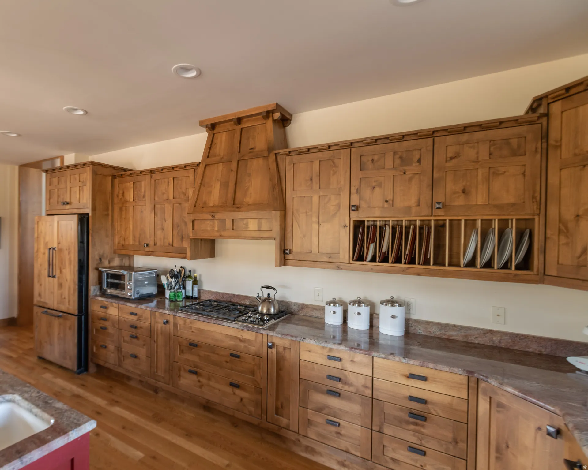 Kitchen featuring wood finish cabinets, refrigerator, light wood-style flooring, dark stone counters, and recessed lighting