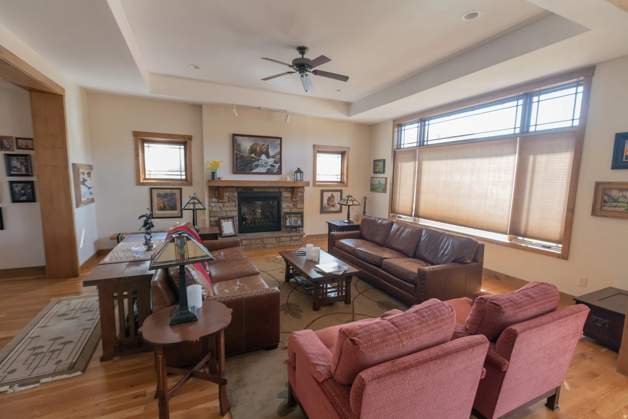 Living area featuring a tray ceiling, a ceiling fan, light wood-type flooring, and a fireplace