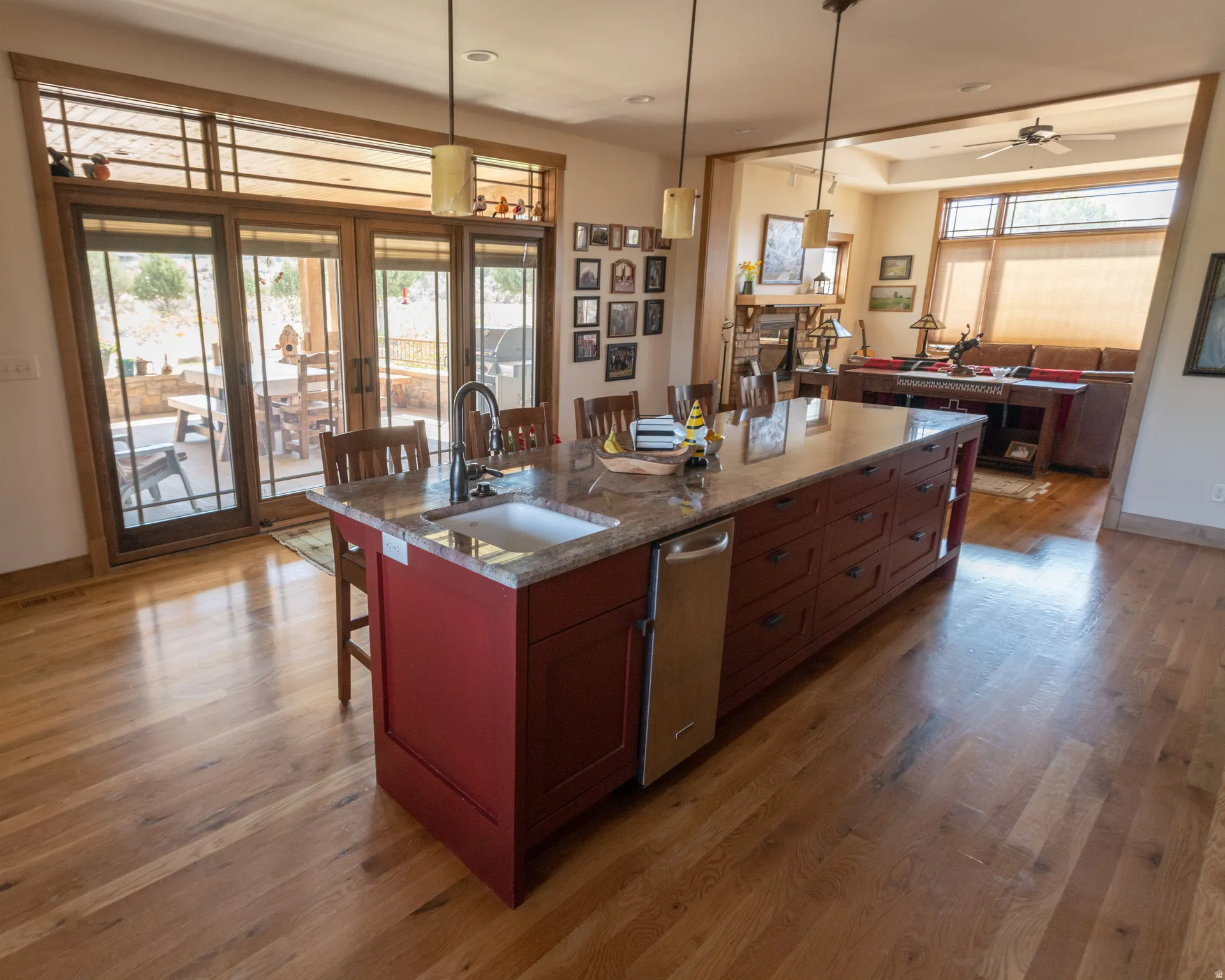 Kitchen with a breakfast bar, pendant lighting, dark stone counters, light wood-style flooring, and an island with sink