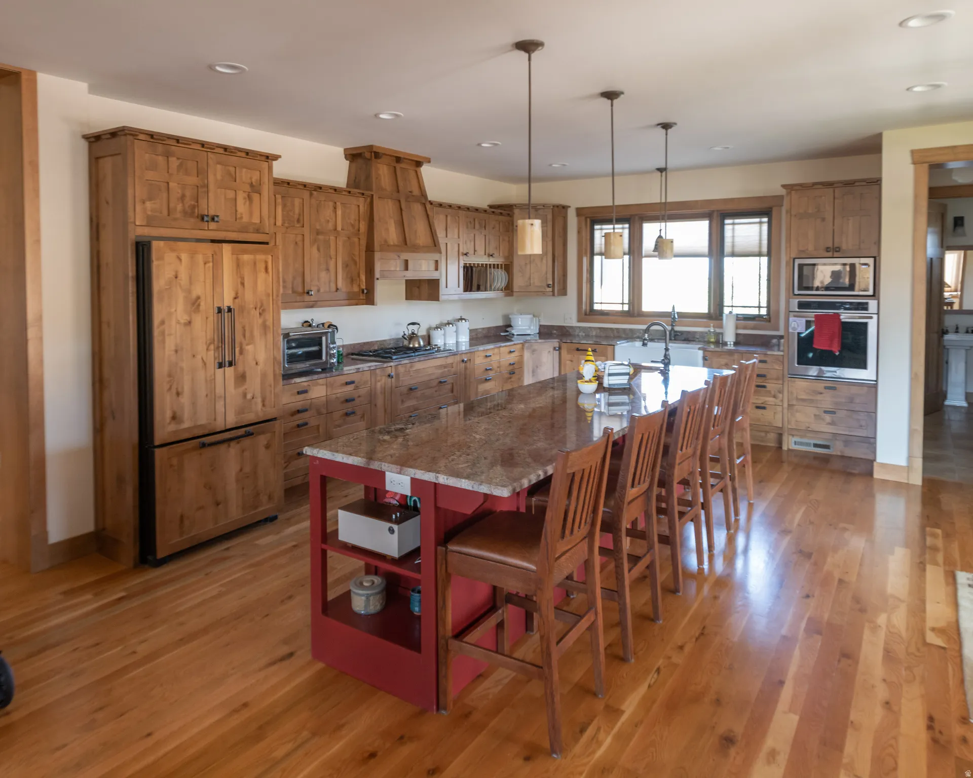 Kitchen featuring built in appliances, an island with sink, wood finish cabinetry, and a kitchen bar
