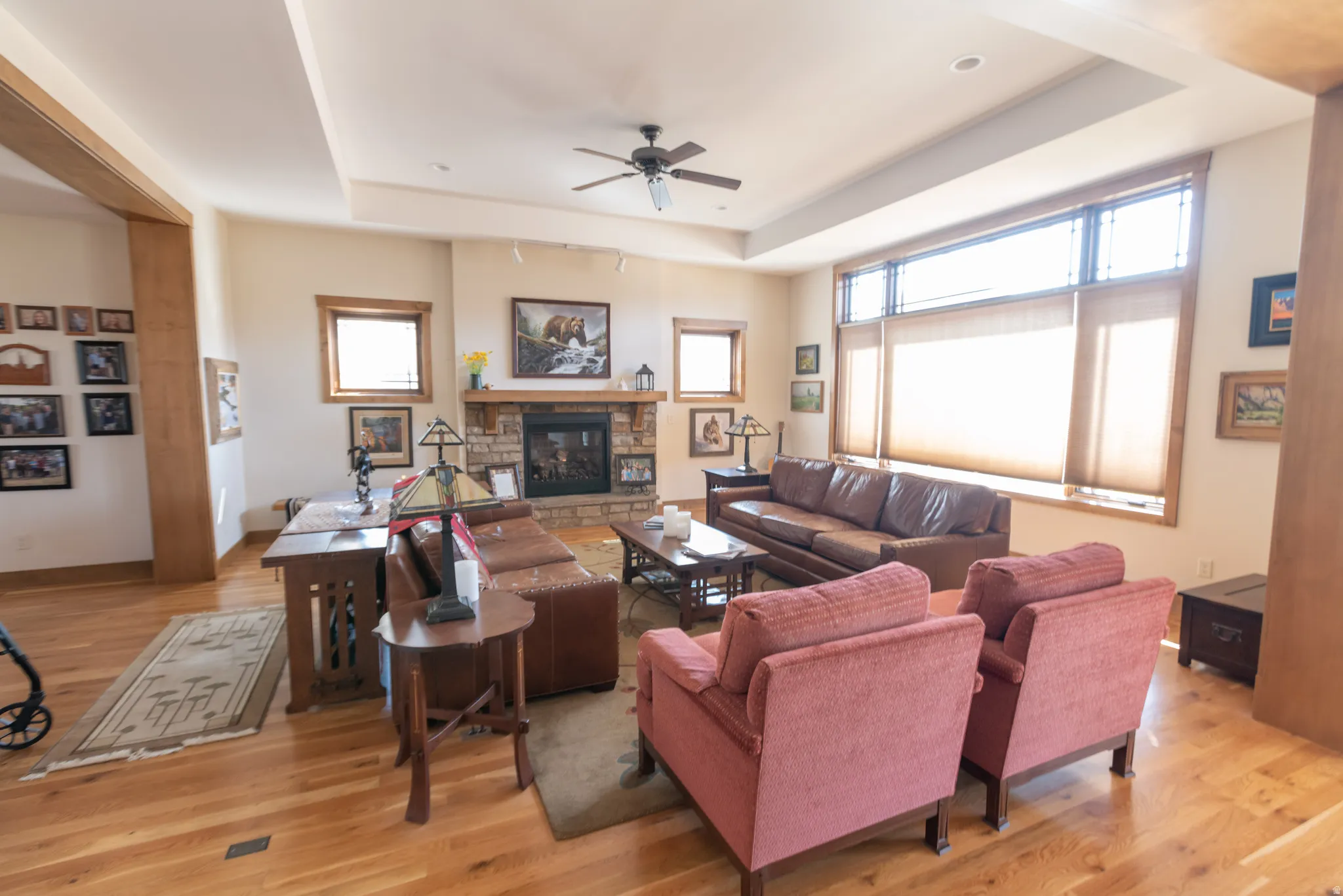 Living area featuring a tray ceiling, ceiling fan, a fireplace, and light wood finished floors