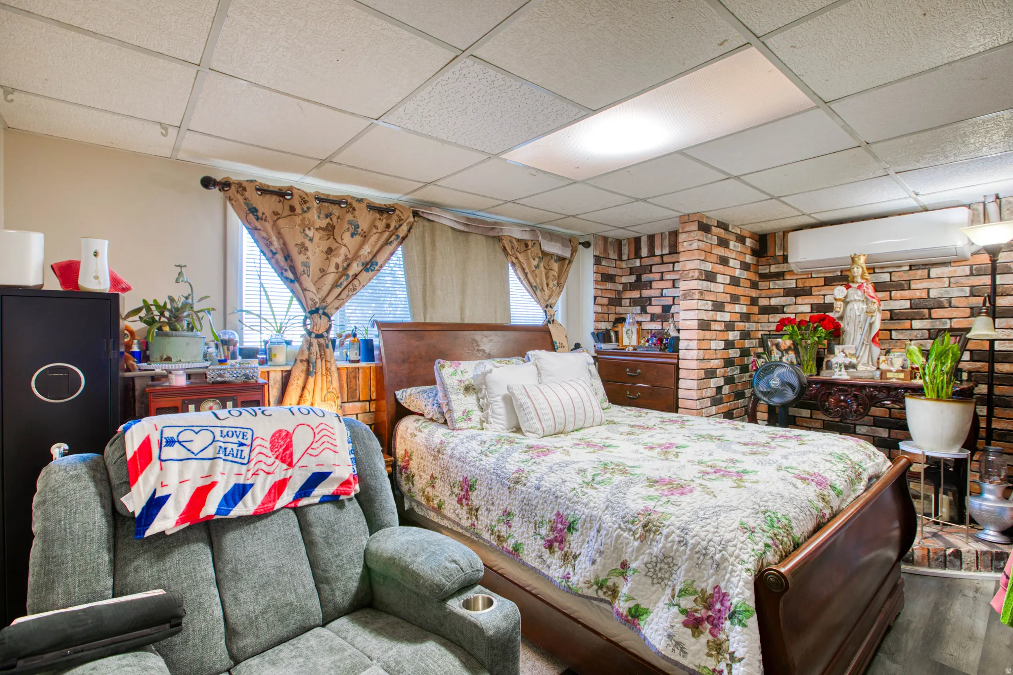 Bedroom with a paneled ceiling, brick wall, and wood finished floors