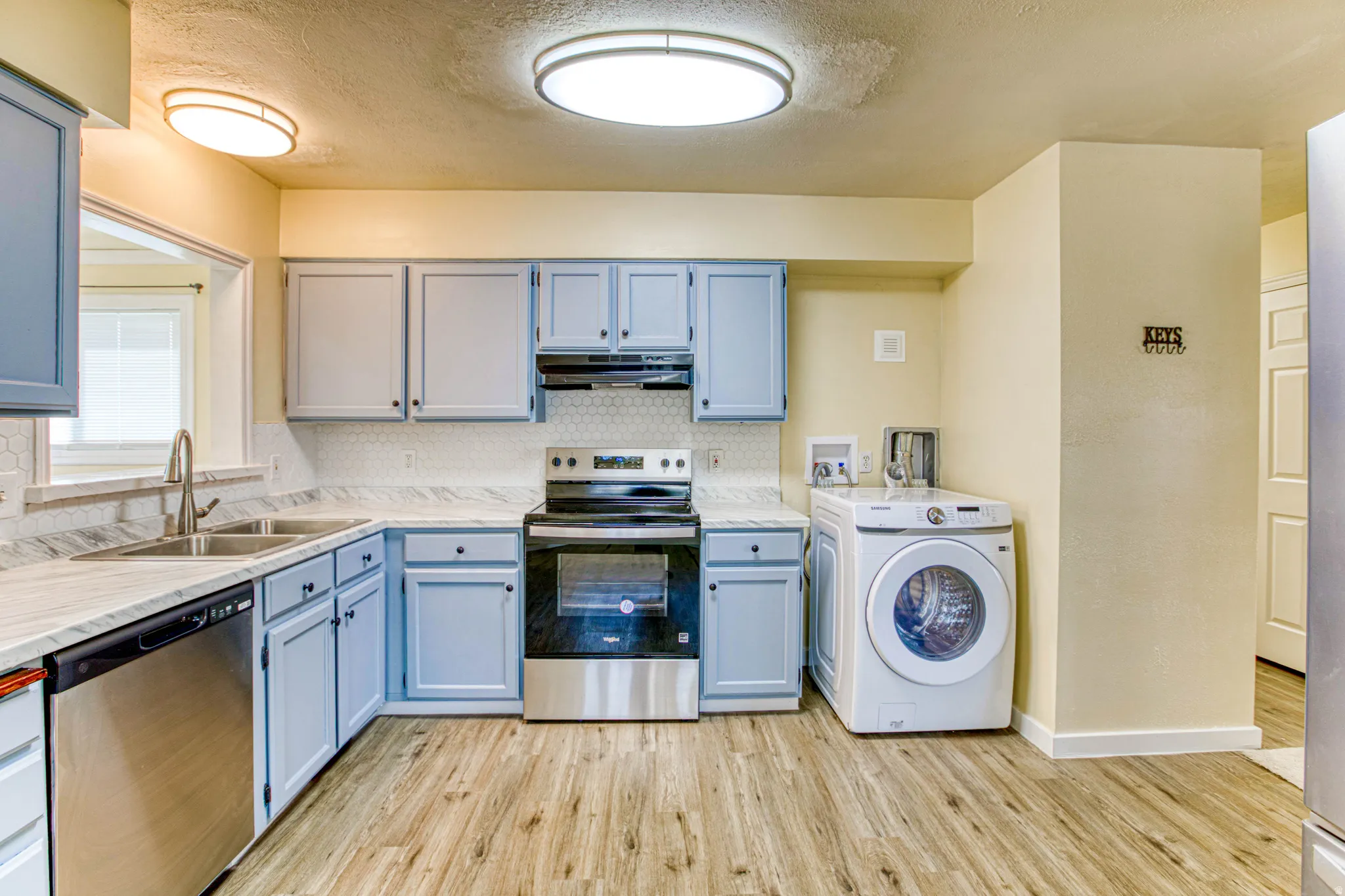 Kitchen featuring stainless steel appliances, washer / dryer, a textured ceiling, light wood-style flooring, and tasteful backsplash