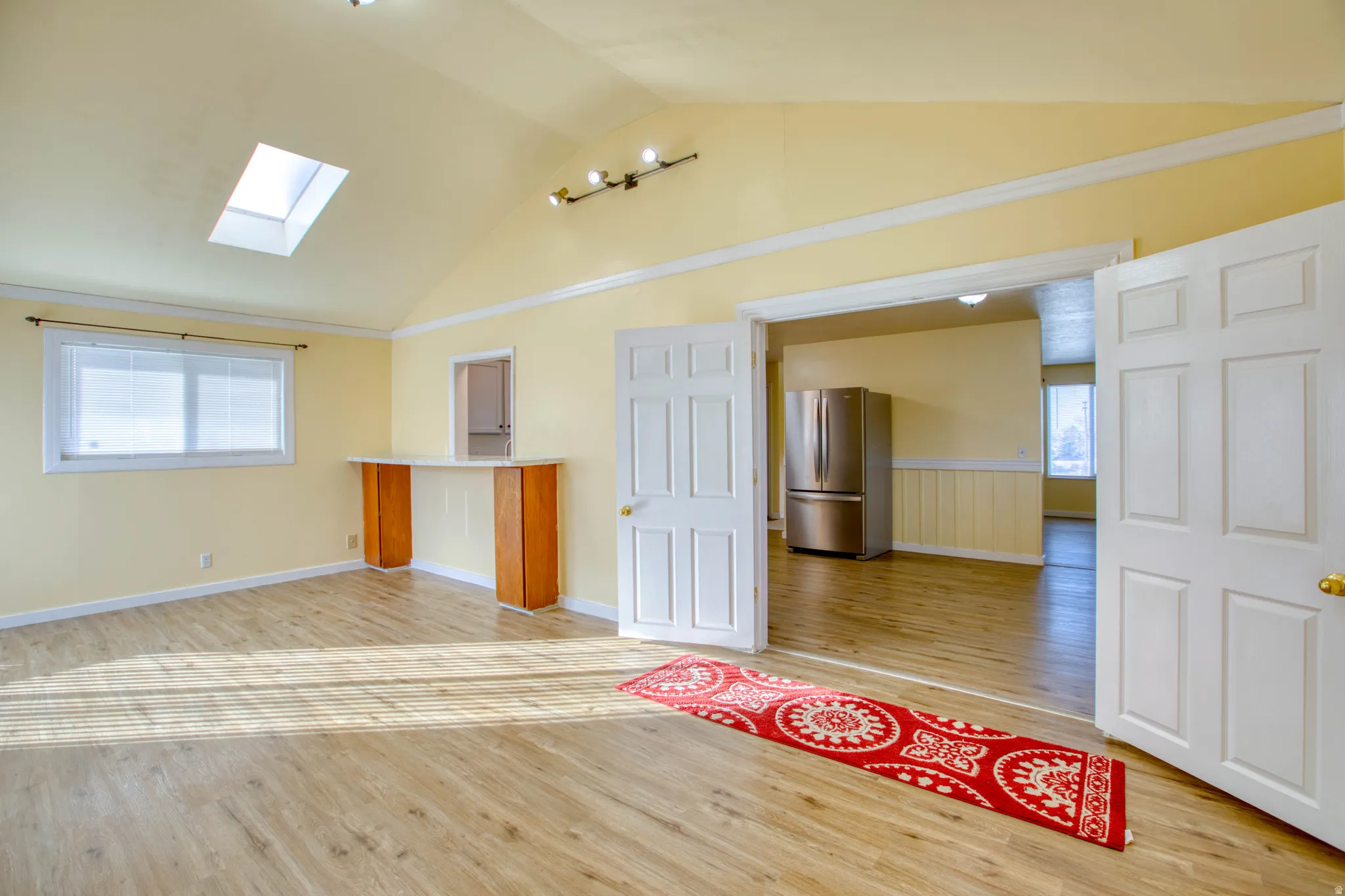 Unfurnished room featuring a skylight, light wood-type flooring, vaulted ceiling, and wainscoting