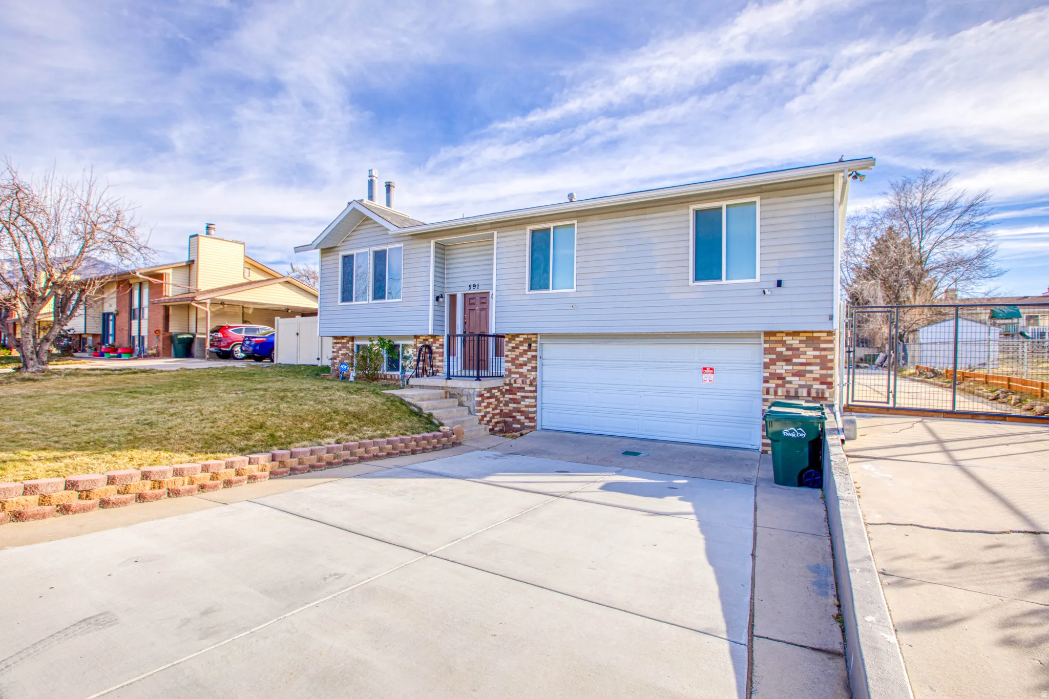 Bi-level home featuring a gate, driveway, an attached garage, and brick siding