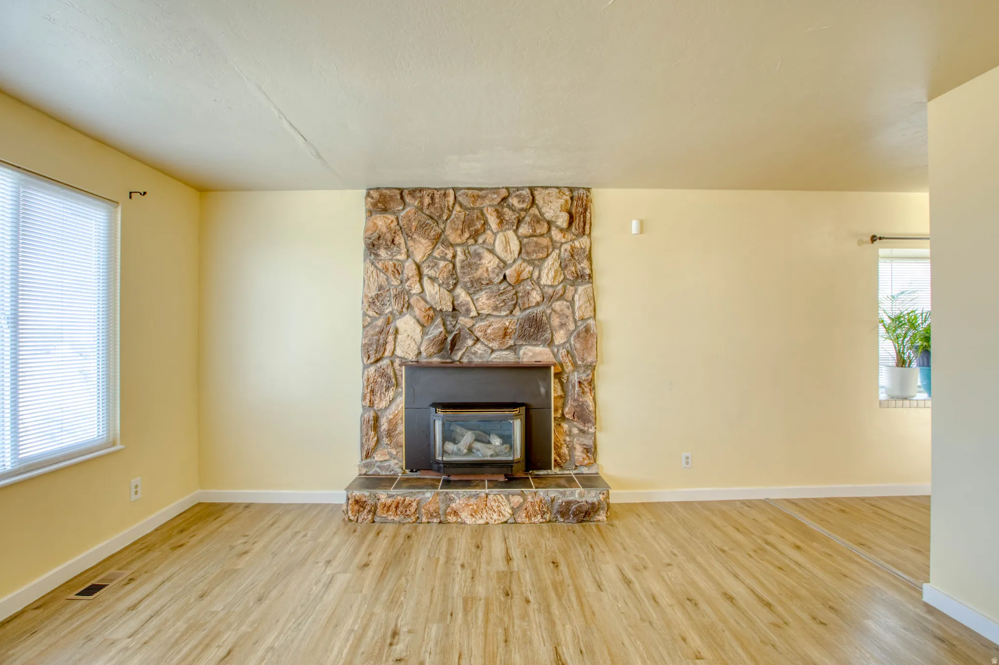 Unfurnished living room featuring a stone fireplace and wood finished floors