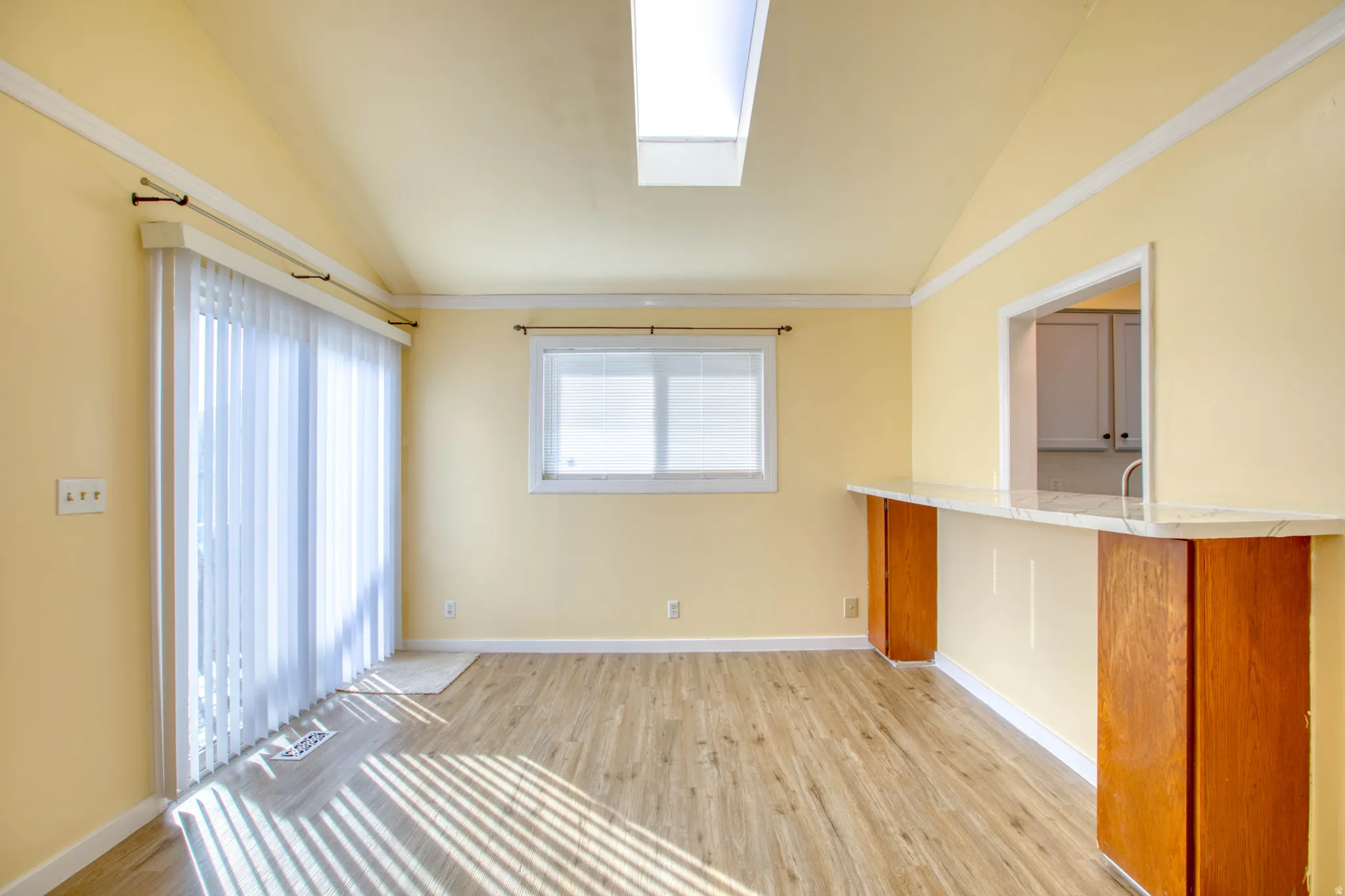 Unfurnished living room featuring vaulted ceiling, light wood-style floors, and a skylight