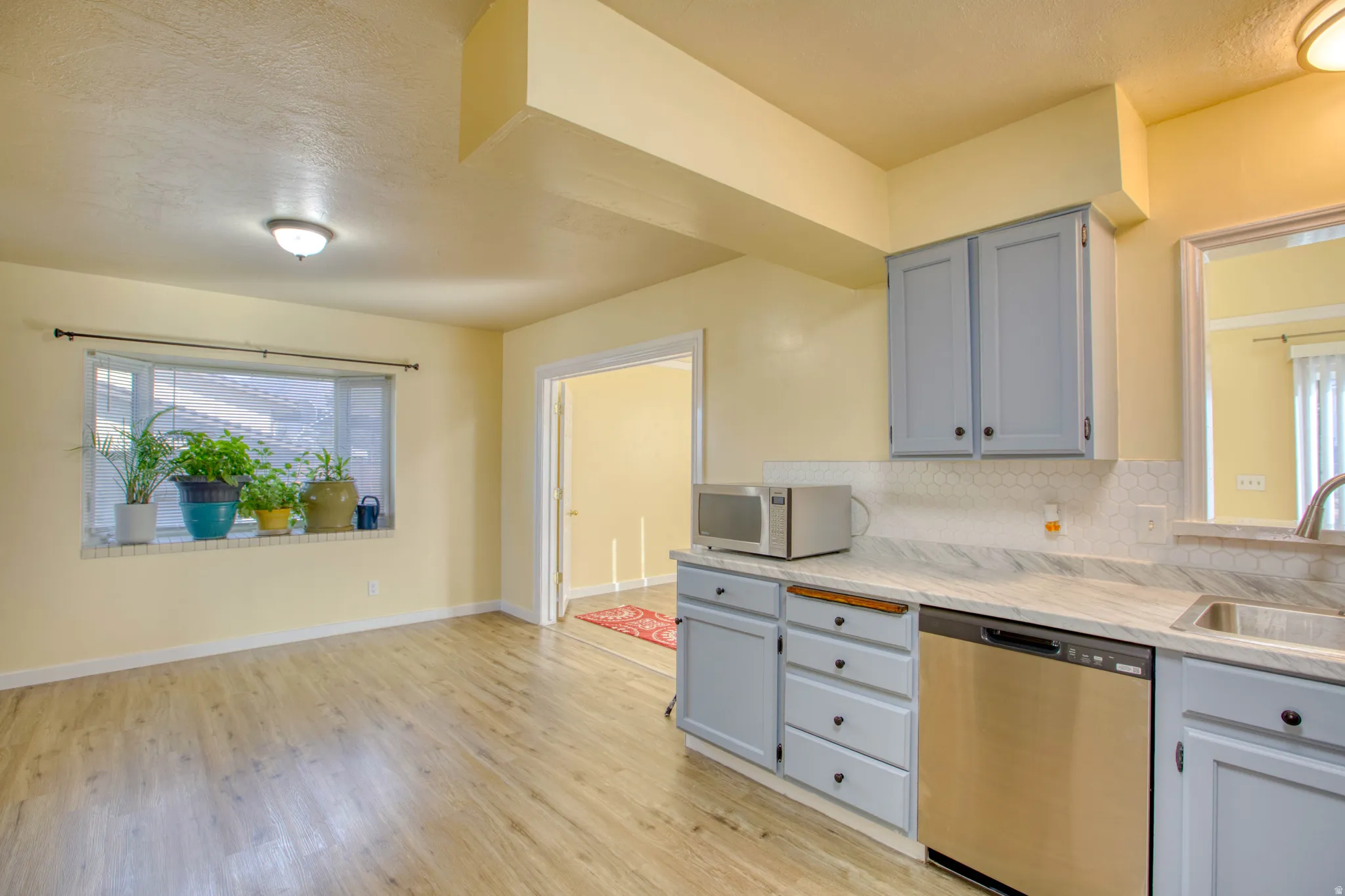 Kitchen featuring gray cabinetry, stainless steel appliances, decorative backsplash, light wood-type flooring, and a textured ceiling